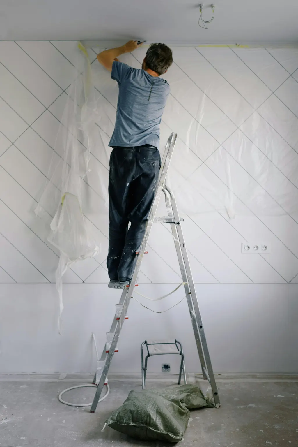 Handwerker auf der Leiter bearbeitet den Übergang zwischen Wand und Decke