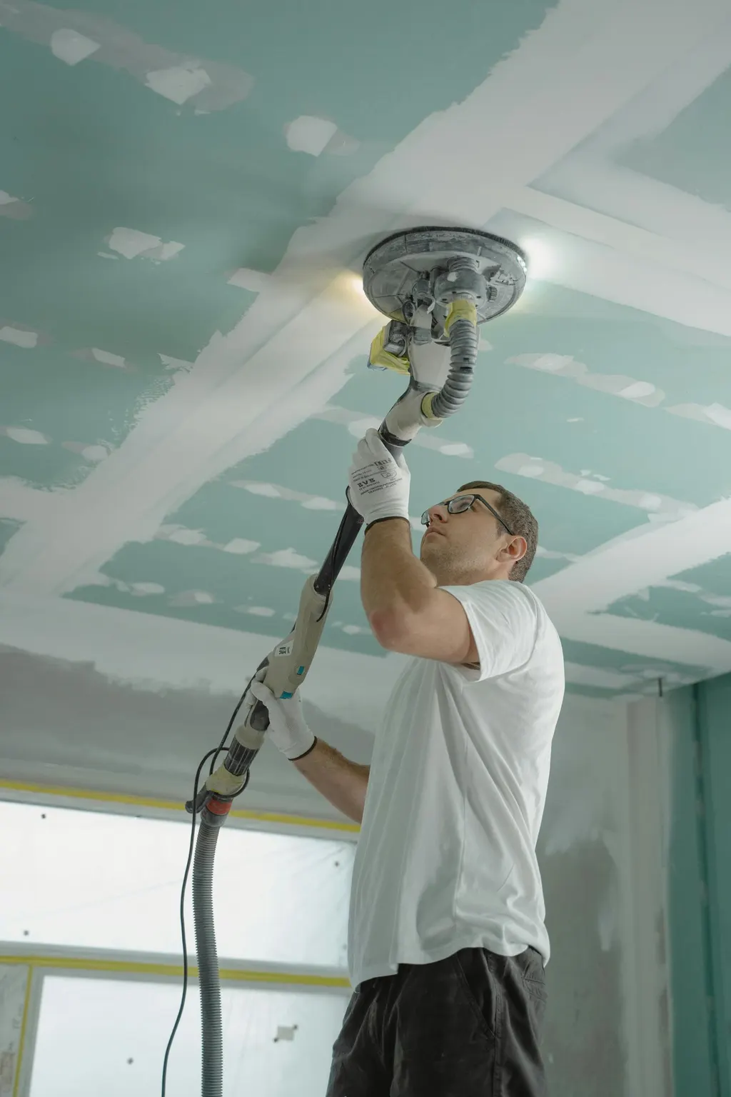 Handwerker schleift eine Gipskartondecke mit dem Langhalsschleifer