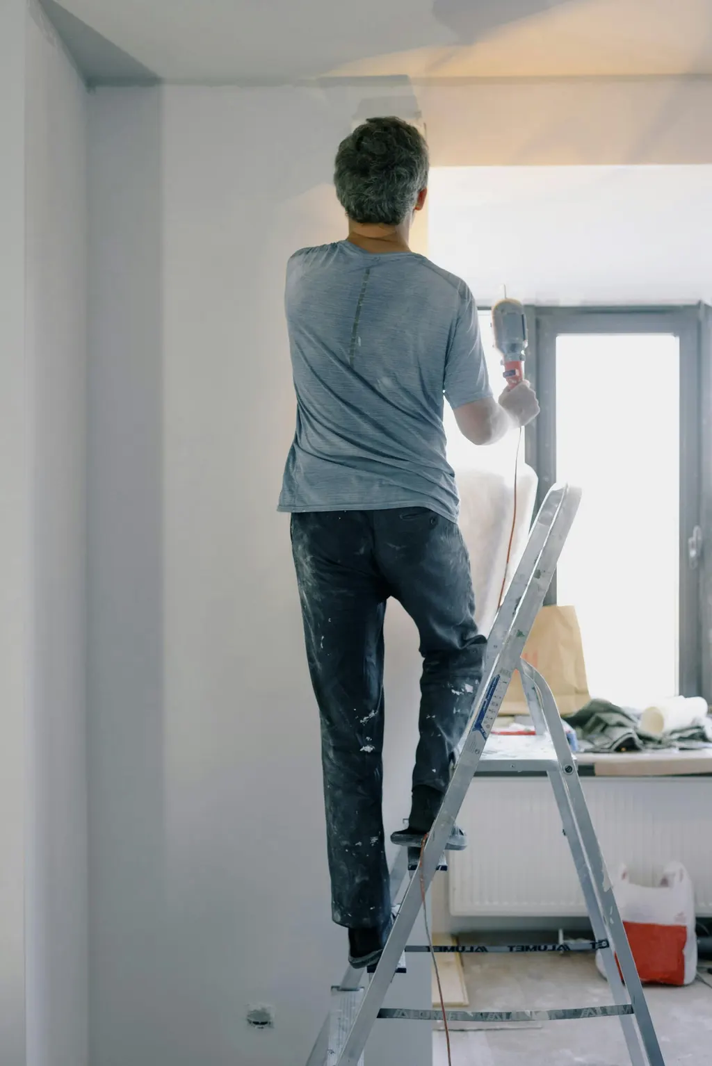 Handwerker auf der Leiter arbeitet an der Wand neben einem Fenster